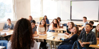 Rear View Of Female High School Teacher Standing At Front Of Class Teaching Lesson