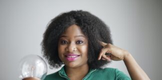 Positive young African American lady holding light bulb in hand on gray background