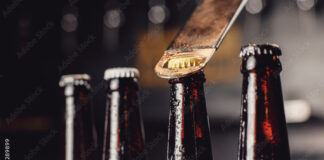 Glass ice cold bottles of beer with opener cap on dark background