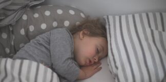 baby in gray long sleeve shirt lying on white and black stripe bed