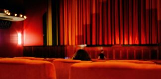 a person sitting in a red chair in front of a red curtain