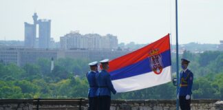 man in black jacket standing near flag of us a during daytime