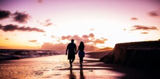 couple holding hands while walking on shore