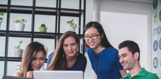 four people watching on white MacBook on top of glass-top table