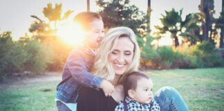 woman holding baby sitting on green grass field under sunset
