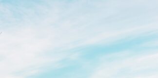 brown and white concrete building near body of water and mountain under white clouds and blue