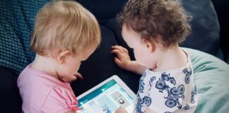 two toddlers sitting on sofa while using tablet computer