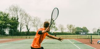 man in orange shirt and black shorts holding black and white tennis racket