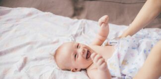 a smiling baby laying on a bed with a woman's arm