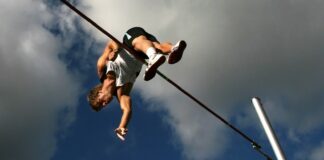 man in white tank top and black shorts hanging on black metal bar under blue sky