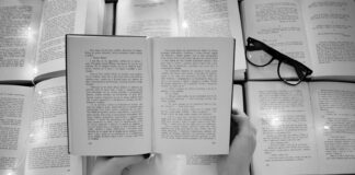 person holding book page with black frame eyeglasses