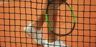 person wearing pair of white low-top sneakers while holding Wilson tennis racket