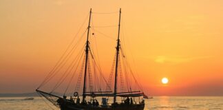 black and white sailboat in body of water during sunset