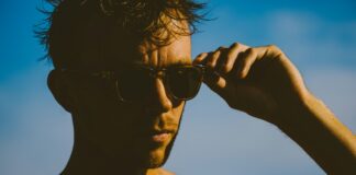man wearing black sunglasses holding black smartphone during daytime