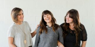 3 women smiling and standing beside white wall