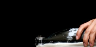 person pouring milk on clear drinking glass