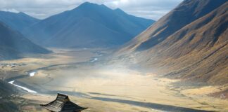 red and brown wooden house near green field viewing mountain under blue and gray skies