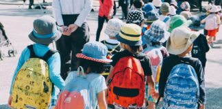 group of people wearing white and orange backpacks walking on gray concrete pavement during daytime