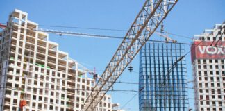 A train traveling past tall buildings under a blue sky