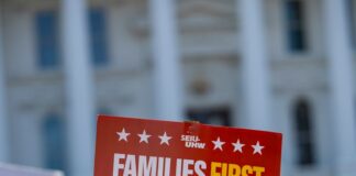 Protest signs reading 'families first, not billionaires' and 'wake america'