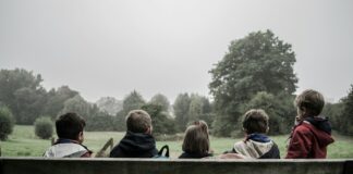 five children sitting on bench front of trees