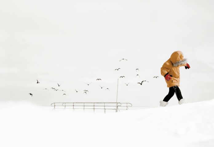 person in orange jacket and black pants walking on snow covered ground during daytime