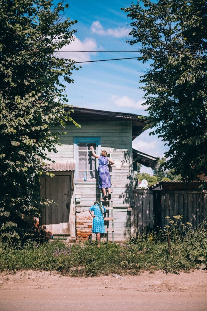 Two women washing a house exterior on a ladder.