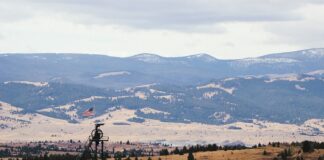 brown and white house on green grass field near mountain under white clouds during daytime