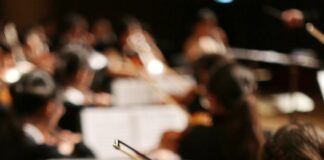 An orchestra performs, focusing on the sheet music.