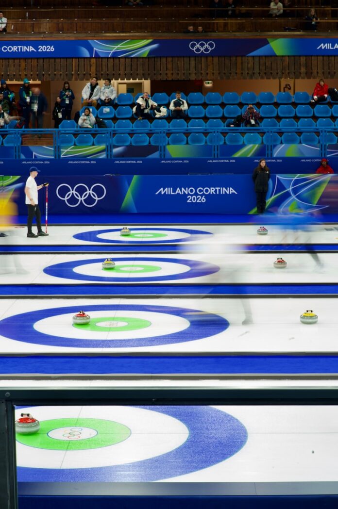 Curling match with athletes sliding stones on ice.