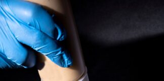 a person in blue gloves is putting ketchup on a sandwich