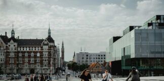 two people biking and other people walking on pathway near buildings under white and blue sky