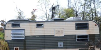 Old camper trailer sits abandoned in overgrown grass.