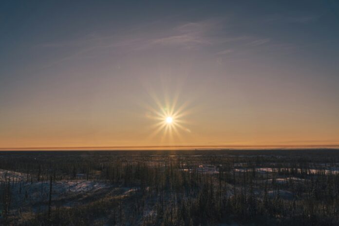 the sun is setting over a snowy field