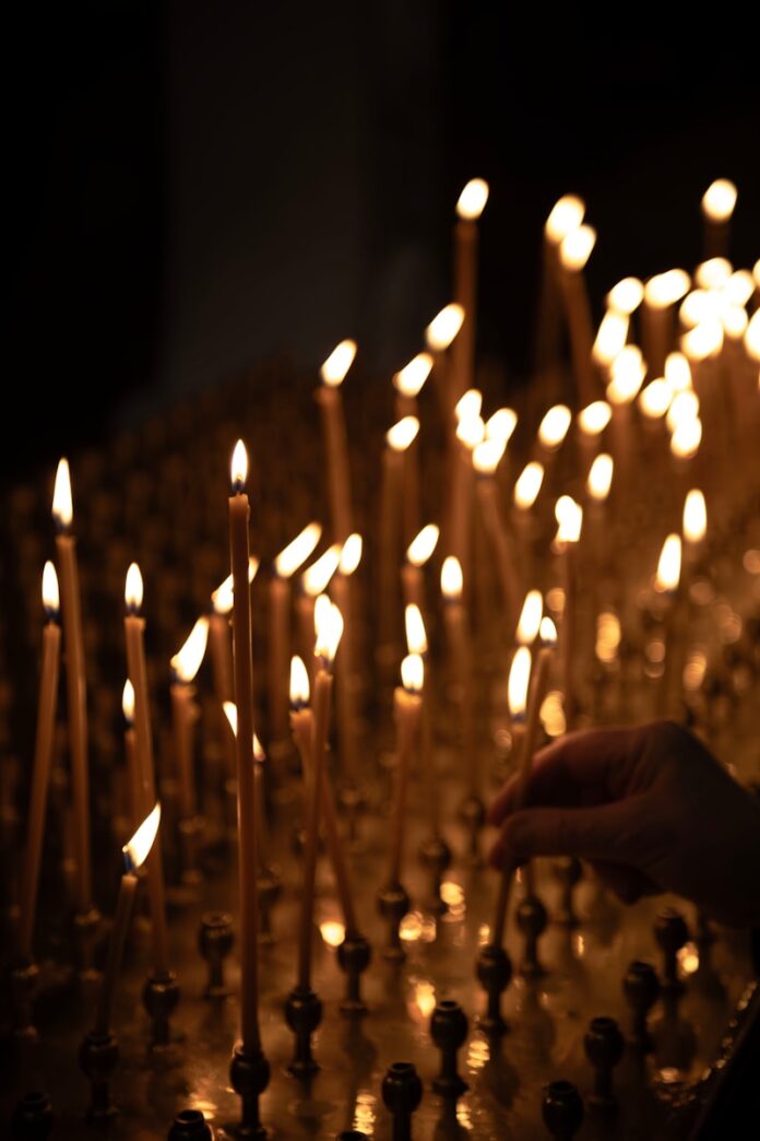 A hand lighting a candle in a dark room.