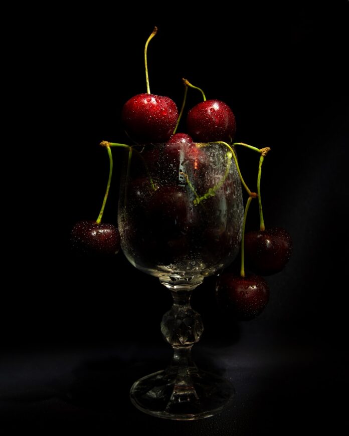 a glass filled with cherries sitting on top of a table