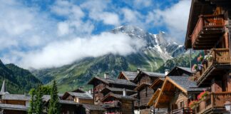 brown wooden houses near green trees and mountain under white clouds during daytime
