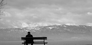 grayscale photo of man sitting on bench