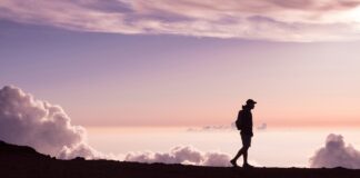 silhouette of person walking under white clouds