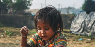 boy in orange and blue stripe shirt sitting on sand during daytime