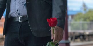 man in black suit holding red rose