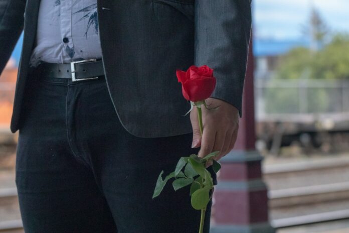 man in black suit holding red rose