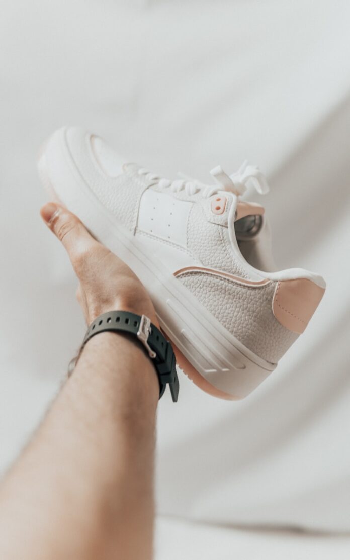 a person holding onto a white tennis shoe